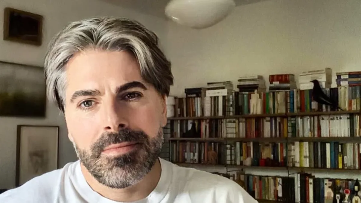 Maurice Munteanu, în tricou alb, într-o încăpere cu rafturi pline de cărți.